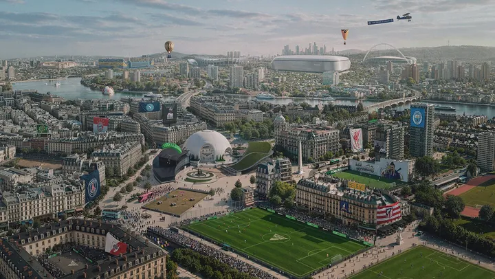 Vista aérea de una ciudad junto a un río, con canchas de fútbol de todos los tamaños entre sus calles, un estadio con cúpula blanca en el centro y, en el cielo, un globo aerostático y un avión que remolca una pancarta