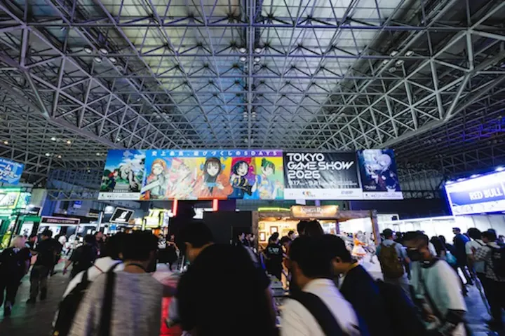 幕張メッセ展示ホールの鉄骨の天井の下に東京ゲームショウ2026の大きな横断幕が掲げられ、通路を来場者が埋めている